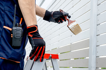 Male painter or decorator hand in protective gloves holding paintbrush while standing on the ladder...