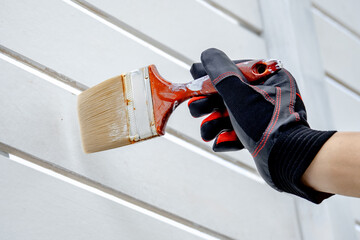 Male painter hand in protective gloves holding paintbrush painting white acrylic color on wooden...