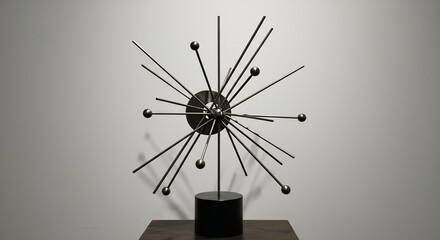 Dark metal starburst sculpture with radiating rods and spheres on a black base against a light grey wall