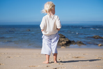 Little blonde European girl walking on an empty sandy beach in Portugal