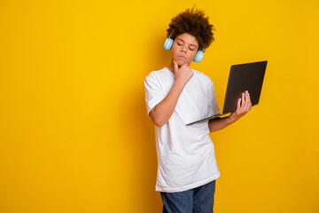 Teenage boy with curly hair in a casual white T-shirt using a laptop against a bright yellow...