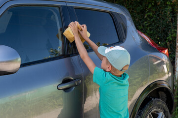 Little boy washing a car with sponge outdoors on a sunny day in summer. concept of helping chores
