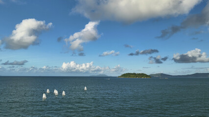 Aerial view of white sails dancing across the deep blue sea, mirroring the fluffy clouds above, near the verdant island, Santa Catarina, California, United States.