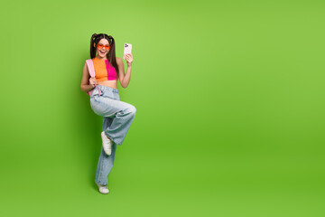 Fashionable young female student with pigtails taking selfie on a smartphone against a bright green...