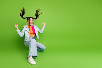 Energetic young woman in trendy casual attire posing playfully against a vibrant green background...