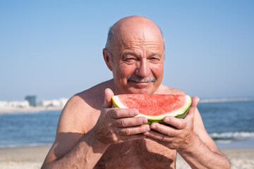 Elderly Spanish man eating watermelon on the beach