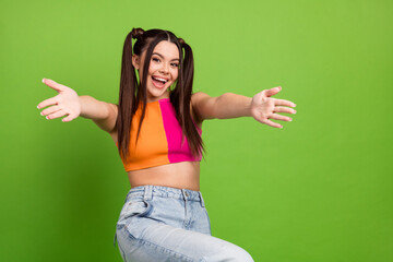 Cheerful young woman with ponytails in colorful outfit posing on a vibrant green background...