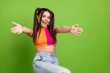 Fotobehang Cheerful young woman with ponytails in colorful outfit posing on a vibrant green background spreading joy © deagreez