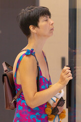A woman wearing a stunning pink and blue dress is elegantly standing in front of a large,...