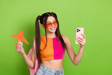 Young woman with vibrant outfit holding travel prop and smartphone against colorful background...