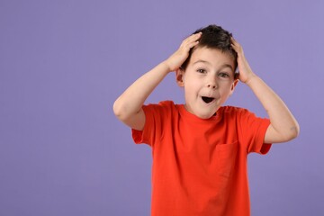 Portrait of surprised boy on purple background, space for text