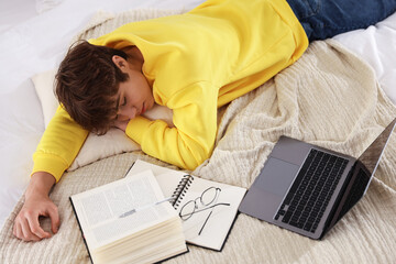 Tired teenage student sleeping near books and laptop on bed at home, above view
