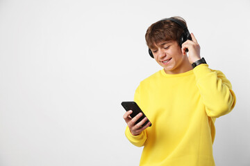 Fototapeta premium Smiling teenage boy in headphones with smartphone on light grey background. Space for text
