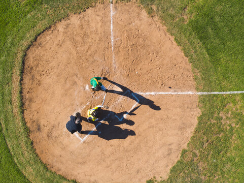 Diverse baseball players and umpire standing at home plate on baseball field holding bat and mitt