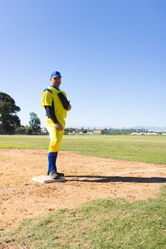 Male baseball player in uniform standing on first base at park holding baseball glove, copy space