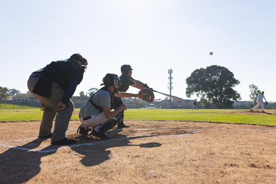 Mature adult white male batter swinging wooden bat at ballpark diamond home plate tracking baseball