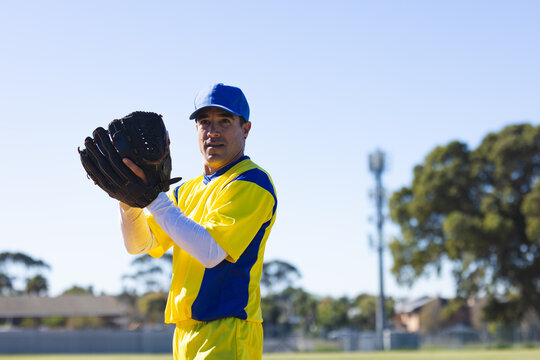 Male baseball player wearing bright yellow uniform with matching cap holding glove in park outfield
