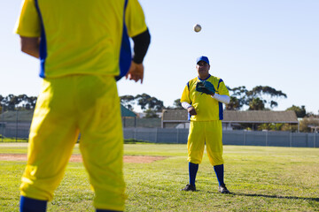 Male baseball player catching baseball wearing yellow and blue uniform on grassy field with fence