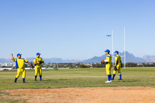 Diverse male teammates in yellow-blue uniforms standing on infield holding gloves under rugby posts