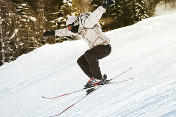 Young male skier training in white jacket black pants jumps off freestyle on snowy slope mid-air...