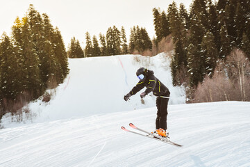 Young male skier training in black outfit pants jumps off freestyle on snowy slope mid-air trick...