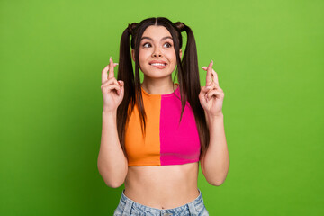 Cheerful young girl with crossed fingers on vibrant green backdrop expressing hope and anticipation...