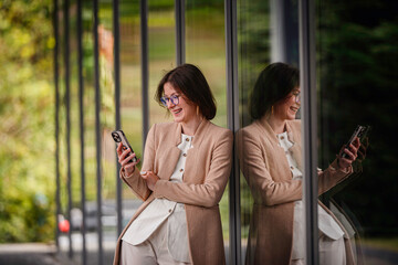 Laughing Businesswoman Reading Phone Message by Glass Wall