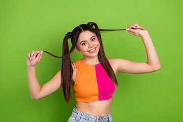 Joyful young woman with stylish hairstyle poses playfully on a vivid green background, showcasing...