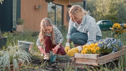 Cute little girl helping her mother gardening flowers in garden. Beautiful mom teaching her kid...