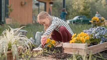 Caucasian little girl cultivating ground after planting plants. Helping her mother working on...