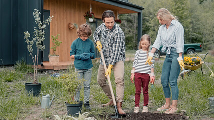 Caucasian family planting plants or tree together in garden. Strong father digging hole while his...