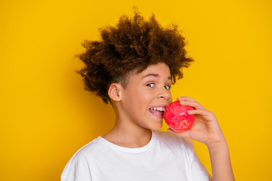 Smiling young boy holding a red apple in front of a vibrant yellow background, expressing joy and energy, wearing a white t-shirt. - Powered by Adobe