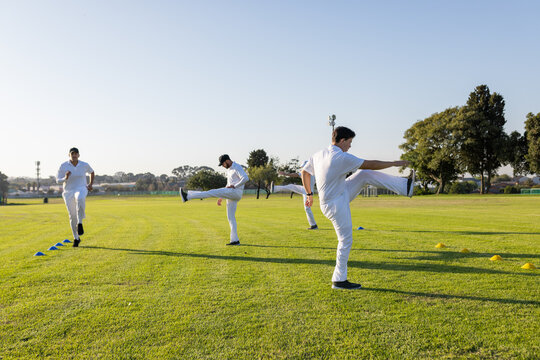 Male athletes performing synchronized high-leg kicks on grass training field with cones, copy space
