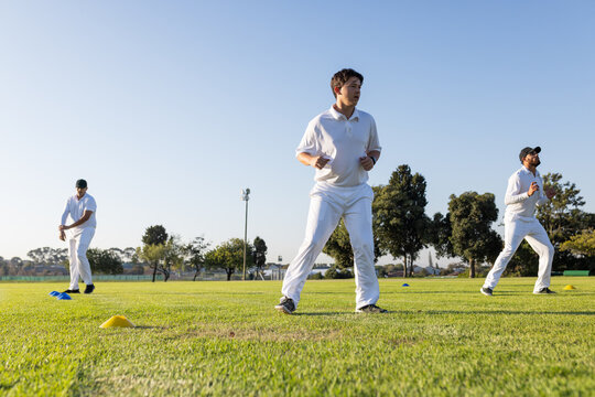 Male cricket teammates warming up on trimmed grass field with yellow cone markers