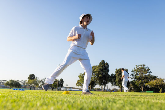 Male cricket teammates performing warm-up strides in white uniforms on field beside training cones