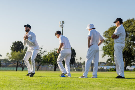 Male cricket players practicing bowling, resetting marker by floodlight tower on grass pitch