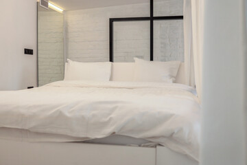 Minimalist bedroom with white bedding and industrial-style glass partition. Soft lighting and white...