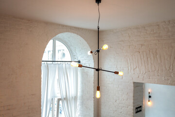 Modern chandelier with exposed bulbs hanging from the ceiling in a white brick interior with arched...
