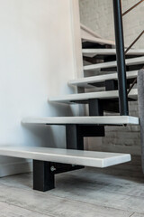 Close-up of modern minimalist staircase design with white wooden steps and black metal supports....