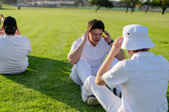Male teammates sitting on grass field performing sit-up drills with bucket hat and wristwatch