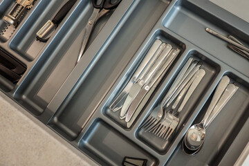 Close-up of neatly organized stainless steel forks, spoons, and knives in a gray kitchen drawer...