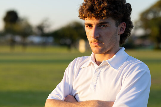 Adult male crossing arms on field at sunset wearing white collared polo shirt, copy space