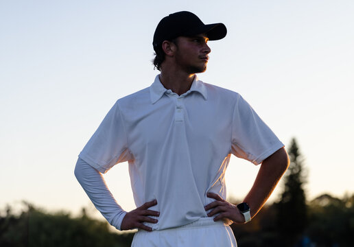 Male golfer standing with hands on hips on golf fairway at sunset wearing baseball cap, smartwatch