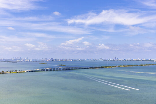 Aerial view of the Julia Tuttle Causeway stretching across Biscayne Bay under a sky brushed with soft clouds, Miami skyline shimmering in the distance, Miami, Florida, United States.
