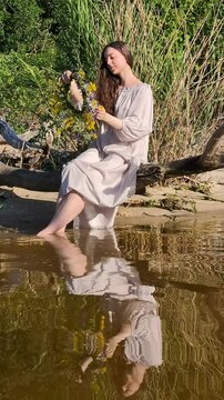 Ukrainian girl in wreath poses near water.
