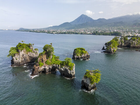 Aerial view of striking rock formations capped with vibrant greenery rise from the sea near Bota Island under the watchful gaze of a majestic mountain, Limbe, South West, Cameroon.