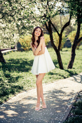 Young woman enjoying a sunny day in a blooming park while wearing a stylish white dress and smiling...