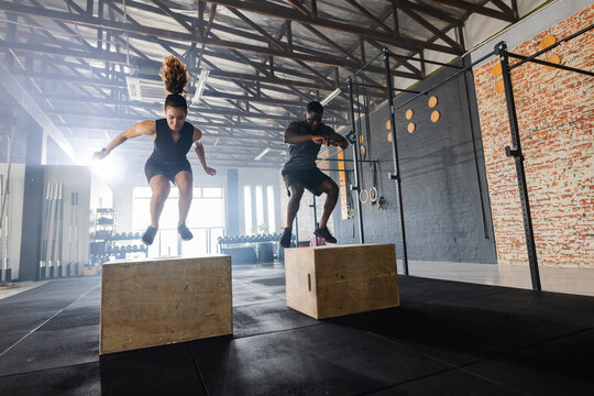 Diverse workout partners in athletic wear jumping onto wooden plyometric boxes in fitness studio - Powered by Adobe