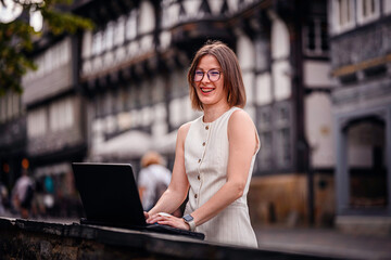 Smiling Woman Working on Laptop in Historic City Setting