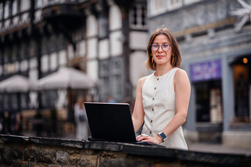 Smiling Woman Working on Laptop in Historic City Setting